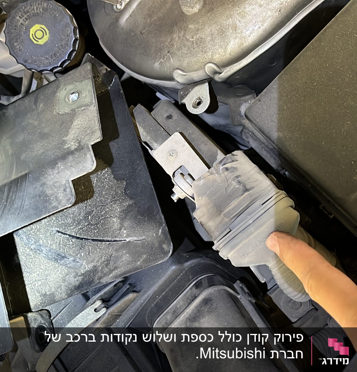 יד מצביעה על חלק במנוע רכב עם מכסה פלסטיק